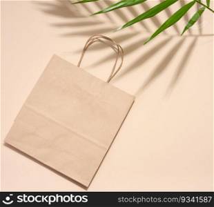 Empty disposable brown kraft paper bag with handles on beige background, eco packaging, zero waste