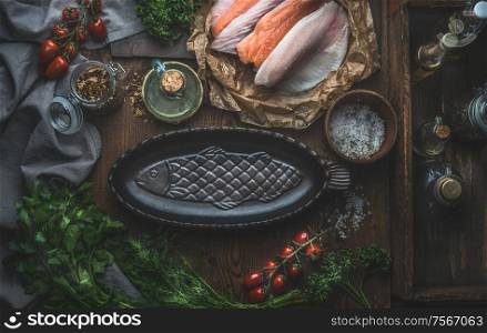 Empty fish backing pan on dark rustic kitchen table background with various fish fillets. Top view