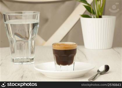 empty glass and a cup of coffee with a spoon on a white table with a flower. cup of coffee on the table