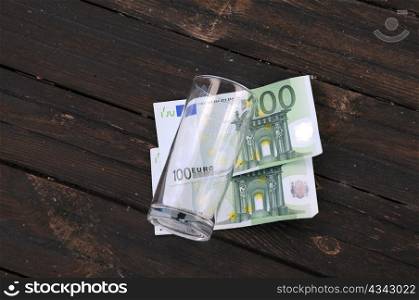Empty glass and one hundred Euro banknotes on wooden table