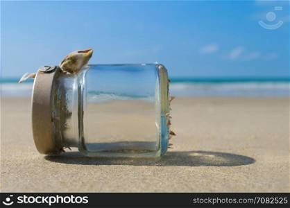Empty glass bottle on sandy beach with blue sky and sea