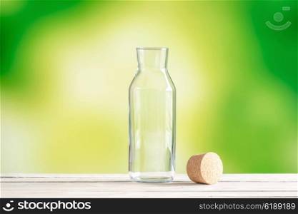 Empty glass bottle with a cork on green background