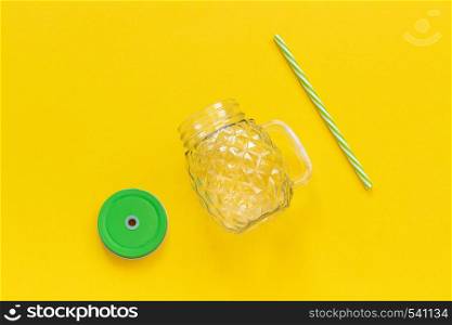 Empty glass jar in form of pineapple with green lid and straw for fruit or vegetable smoothies, cocktails and other beverages on yellow background. Top view Copy space Template.. Empty glass jar in form of pineapple with green lid and straw for fruit or vegetable smoothies, cocktails and other beverages on yellow background. Top view Copy space Template
