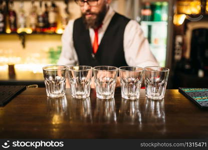 Empty glasses on wooden bar counter, bartender working on background