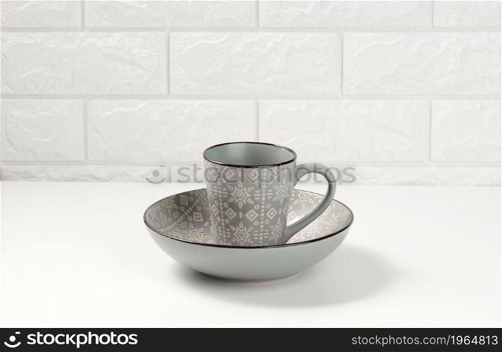empty gray ceramic soup plate and empty cup on white table, utensils