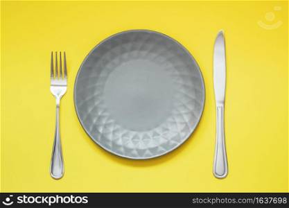 Empty gray plate and cutlery on yellow background. Trending Color of the year - Illuminating and Ultimate Gray.. Empty gray plate and cutlery on yellow background. Trending Color of year - Illuminating and Ultimate Gray.