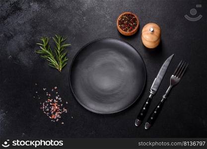 Empty gray plate on a dark background with a knife and fork. Empty round black plate on dark moody black background with copy space