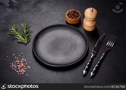 Empty gray plate on a dark background with a knife and fork. Empty round black plate on dark moody black background with copy space