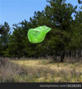 empty green garbage bag flies against the background of green pines in the forest on a summer sunny day. empty green garbage bag flies against the background of green pi