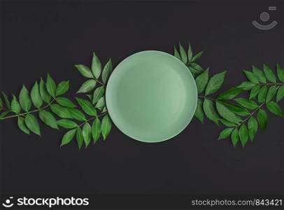 Empty green plate on green leaves and black table. Above view of food background. Mockup. Flat lay of an empty dish on tree twigs. Empty tableware.