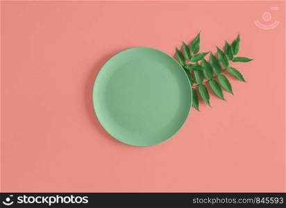 Empty green platter on green tree twigs on a coral colored background. Above view of minimal food background. Flat lay of an empty dinner plate.