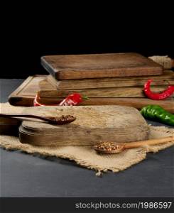 empty kitchen brown wooden cutting board on black table, next to spoons with spice and fresh chili, black background