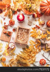 Empty kraft paper box on white blanket with autumn branches and fall leaves, cappuccino, cosmetic products, burning candle, pumpkin and rowan. Zero waste, eco friendly packaging. Beauty box. Top view