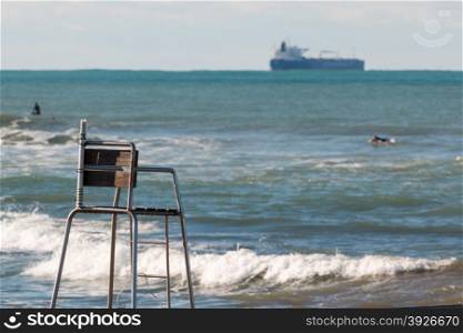 empty lifeguard chair, surfers in sea and container ship in background