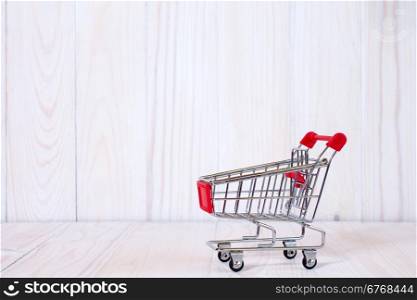 Empty mini shopping cart against white wooden background