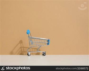empty miniature shopping cart on brown background. Seasonal sale, copy space, online shopping