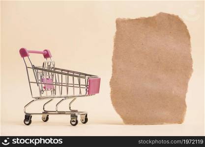empty miniature shopping trolley near torn paper piece against colored backdrop. High resolution photo. empty miniature shopping trolley near torn paper piece against colored backdrop. High quality photo