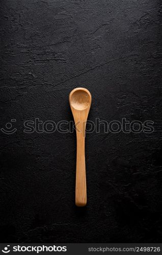 Empty new clean small bamboo wooden spoon on black dark table background top view flat lay.