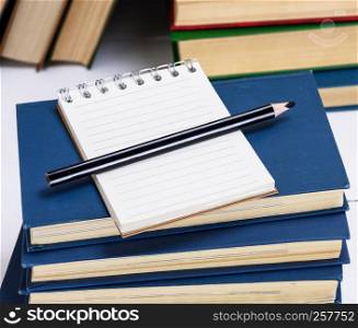 empty notebook with white sheets and a black pencil are on a stack of books