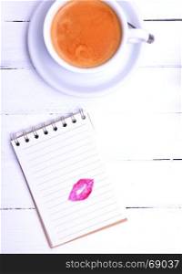 Empty notepad with a lipstick print and a cappuccino, top view