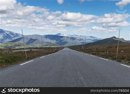 empty nroad in norway with Poles for the snow blades and mountains with snwo as background in July on the valdresfya nature area. empty road in norway