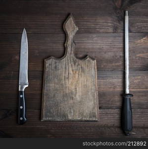 empty old brown wooden cutting board and knife with sharpening on the table, top view