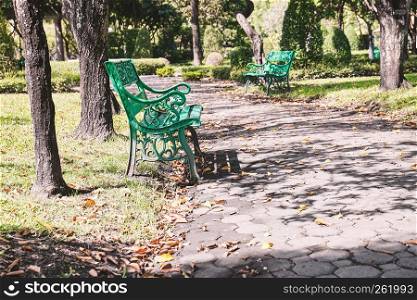 Empty old green bench in the garden with warm sunlight. Relaxation corner, chairs in the city park.