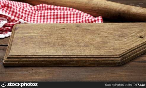 empty old wooden cutting board and folded red and white cotton kitchen napkin on a wooden brown background, top view