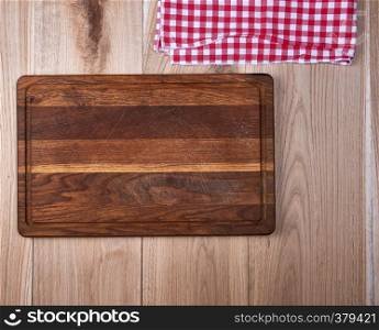 Empty old wooden kitchen cutting board and a red towel on a brown table, the view from the top