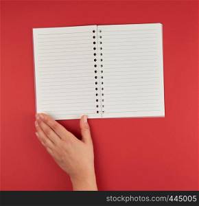 empty open notebook and a female hand, red background, top view