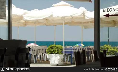 Empty outdoor cafe on the beach with big sun umbrellas and sea in distance