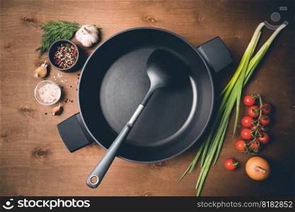 Empty pan on a kitchen table surrounded by vegetarian cuisine ingredients, top view. Empty pan surrounded by vegetarian