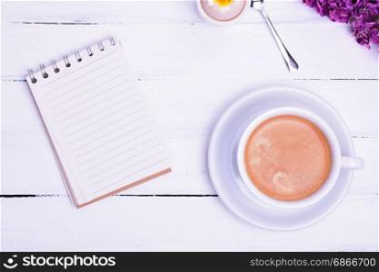 Empty paper notebook and cup of coffee with brown foam, top view