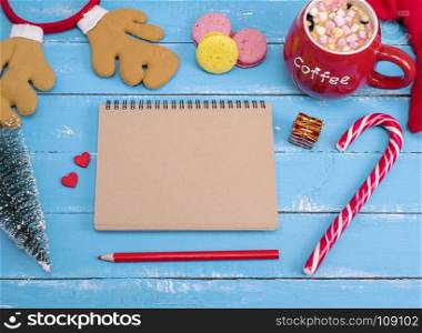 empty paper notebook and cup of hot chocolate with marshmallow on a blue wooden background, top view