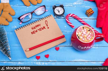 empty paper notebook with red pencil, next is a red cup with coffee and marshmallow on a blue wooden background