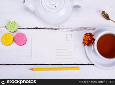 empty paper postcard and cup of tea and saucer on white wooden table, top view