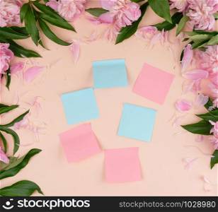 empty paper stickers on a peach background, on the perimeter a bouquet of blooming peonies, top view