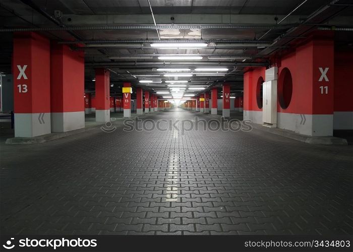 Empty parking garage. Neon lighting, white and red reinforced concrete pillars, grey stone floor.