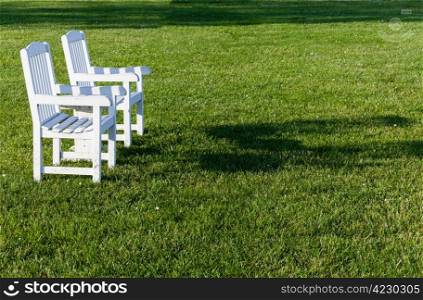 Empty patio chairs sitting on grass lawn in late afternoon sunshine