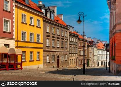 Empty paved street with colorful facades of houses and lantern in the Old Town of Warsaw in the summer sunny day, Poland