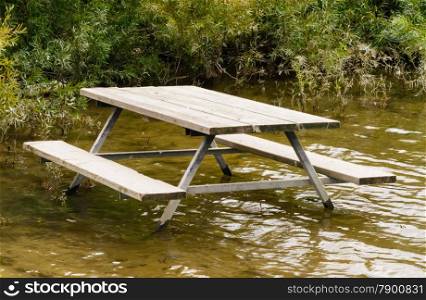 Empty picnic table standing in brown water against green plants.