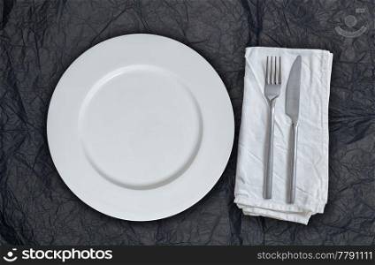 Empty plate and cutlery on black tissue paper.. Empty plate and cutlery on black tissue paper
