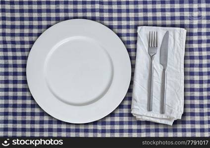 Empty plate and cutlery on blue-white checkered cloth.. Empty plate and cutlery on blue-white checkered cloth