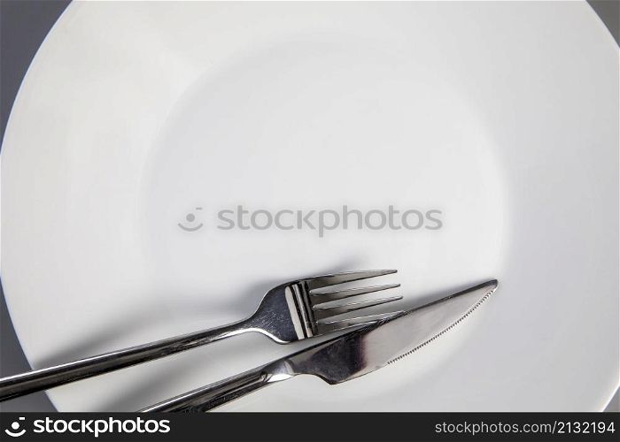 Empty plate with fork and knife on gray background, top view for copy space, food and healthy eating concept space for text. Empty plate with fork and knife on gray background, top view for copy space, food and healthy eating concept