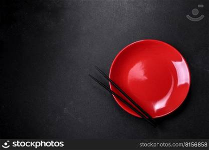 Empty plate with wooden sticks for Asian food on a dark concrete background. Preparation of Asian cuisine. Empty plate with wooden sticks for Asian food on a dark concrete background