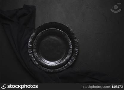 Empty plates and black kitchen towel on a table. Above view of black empty dishes. Black tableware on black table. Black table arrangement.