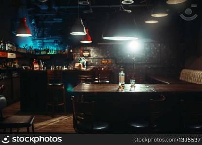 Empty pub, bottle of alcohol and glass on bar counter. Restaurant interior, nobody