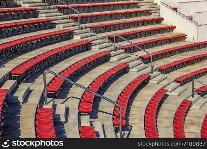 Empty red plastic chairs in the stands of the stadium or amphitheater. Many empty seats for spectators in the stands.