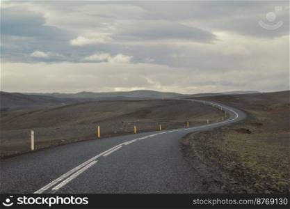 Empty road across hills landscape photo. Beautiful nature scenery photography with cloudy sky on background. Idyllic scene. High quality picture for wallpaper, travel blog, magazine, article. Empty road across hills landscape photo