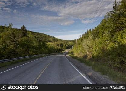 Empty road amidst trees by hills, Ceilidh Trail, Cape Breton Island, Nova Scotia, Canada